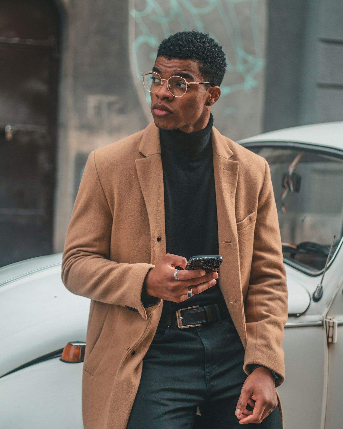 A man standing next to a white car looking at his cell phone