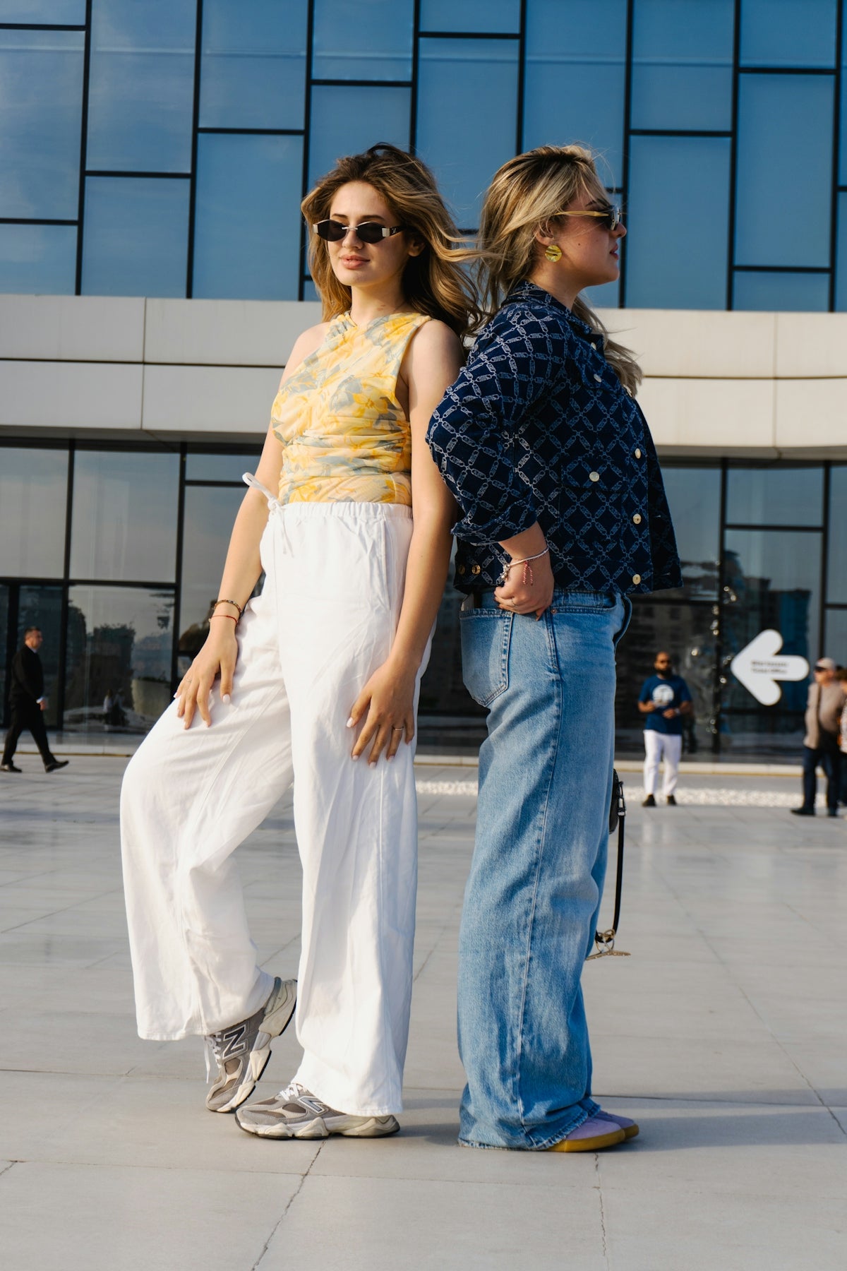 Two young women standing back to back outdoors.